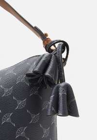 Schwarze Lederhandtasche mit strukturiertem Finish, floralem Muster und einem braunen Tragegurt mit Quastenakzenten.