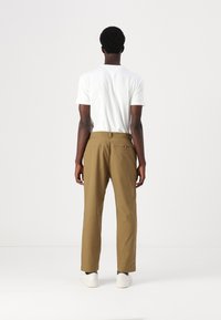 Pantaloni maro cu o croială dreaptă, confecționați dintr-un material țesut, având un buzunar pe spate și asortați cu un tricou alb și adidași albi.