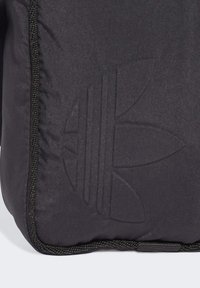 Bolso negro con un logo texturizado que presenta tres rayas, material acolchado suave y detalle de cremallera en contraste a lo largo de los bordes.