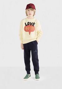 Creme sweatshirt med en rød og sort grafik, der siger "LOVE," marineblå sweatpants og grønne slips-on sko med hvide polka dots. Rød kasket.