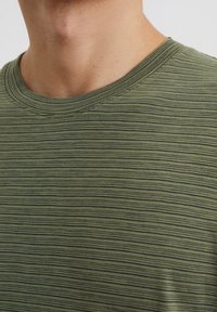 Green striped t-shirt with a round neck, made from soft fabric. Features fine horizontal lines in varying shades of green and black.