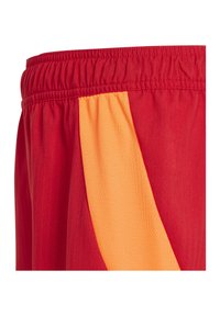 Rode sportshorts met een elastische tailleband en een diagonaal oranje paneel aan de zijkant.