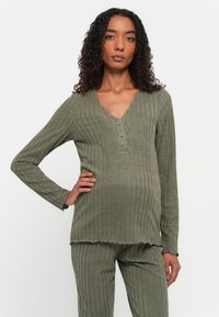 Olivegrünes, geripptes Longsleeve-Oberteil mit V-Ausschnitt und drei Knopfverschluss; kombiniert mit passenden Hosen. Weiche Textur und figurbetontes Design.