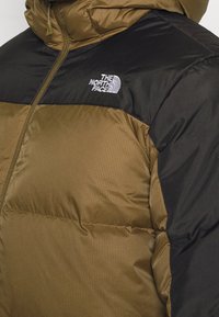 Dunjacka med en strukturerad olivgrön kropp och svart yoke, dragkedjestängning och broderad logotyp på vänster bröst.