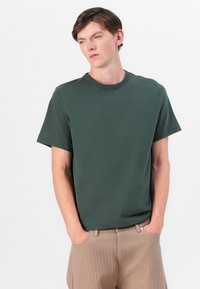 T-shirt à manches courtes vert foncé avec un col rond, fabriqué en coton, coupe décontractée, avec des détails de couture subtils et une texture lisse.