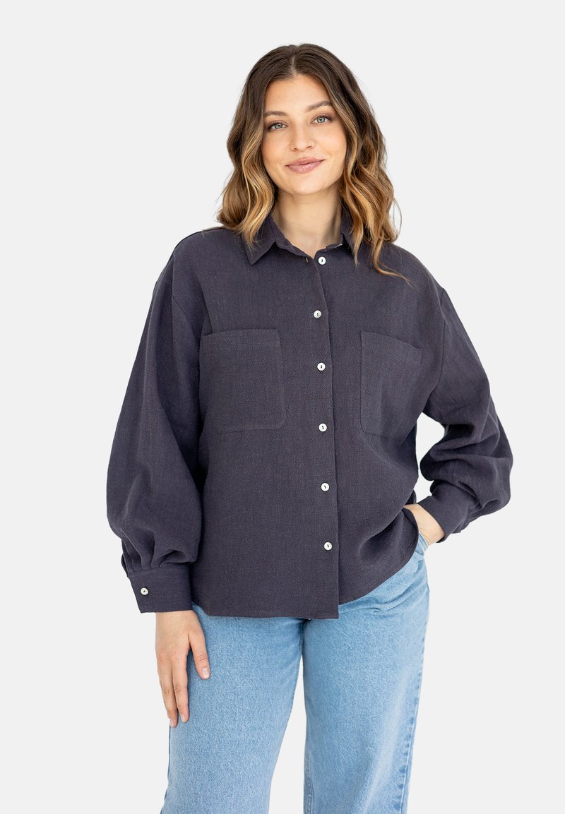 Ciemnoniebieska koszula zapinana na guziki z dwoma kieszeniami na piersi, luźny krój, szerokie rękawy i białe guziki; wykonana z fakturowanej tkaniny.