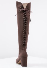 Bota marrón de ante hasta la rodilla con tacón alto, que cuenta con un diseño de cordones en la parte trasera y una puntera afilada.