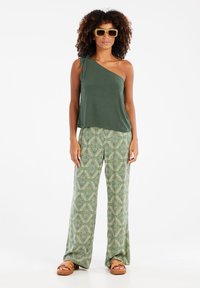Top verde de un solo hombro con detalle de lazo, combinado con pantalones de pierna ancha estampados en verde y amarillo. Sandalias color marrón arena completan el look.