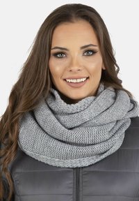 Grijze gebreide sjaal van zacht materiaal, met een chunky weving en opgerolde randen, gedragen over een donkere pufferjack.