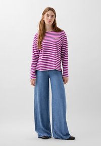 Gestreiftes Langarmhemd in Lila und Weiß, kombiniert mit weit geschnittenen blauen Jeans. Das Hemd hat einen Rundhalsausschnitt und dezente Markenkennzeichnung.