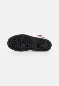 Sola de sapato de borracha preta com padrões de ranhura circulares e lineares. Detalhes em vermelho e branco com o logótipo da Nike em relevo.