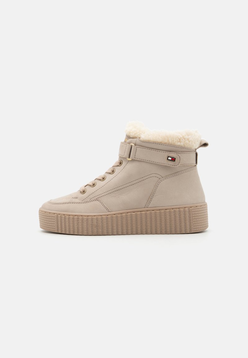 Zapatillas de deporte altas beige, hechas de cuero suave con forro de pelo sintético, que presentan una suela de plataforma texturizada y una correa cerca del tobillo.