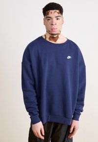 Námořnická modrá mikina Nike se stojáčkem, dlouhými rukávy a bílým logem na hrudi. Disponuje měkkou texturou a uvolněným střihem.