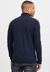 Maglione blu navy a maniche lunghe con colletto alto, polsini e orlo a coste. Texture morbida, design slim fit e cuciture minime.