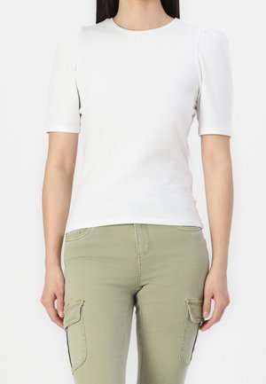 Woman wearing a fitted white short-sleeve top and light green cargo pants with front flap pockets, standing against a plain background.