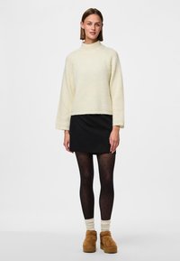 Lettere tekstureret cremet striktrøje med høj krave, sort nederdel, leggings med polka prikkede mønster og brune ruskind ankelstøvler.