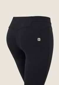 Leggings neri a vita alta con una consistenza liscia, un design con cuciture curve e una piccola etichetta con logo sul retro.