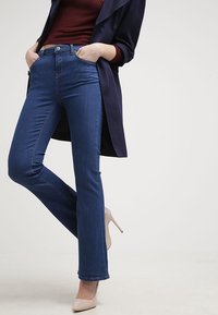 Denimjeans i mörkblått, slim fit, med en klassisk femfickdesign, kombinerat med en figurnära vinröd ribbad topp och en lång marinblå jacka.