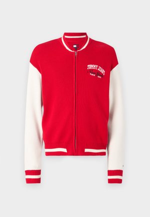 Red and white ribbed knit bomber jacket with a zip closure, featuring a Tommy Jeans logo on the chest and striped details on cuffs and hem.