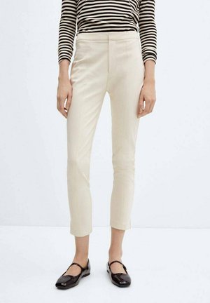 Person iført cremefarvede, slim-fit ankellange bukser, sorte lak-Mary Jane-sko og en langærmet top med sort-hvide striber.