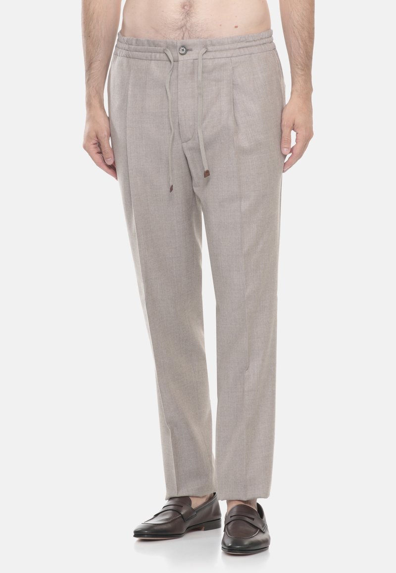 Pantaloni su misura grigio chiaro con vita regolabile e bottone, indossati con mocassini in pelle marrone scuro su un modello maschile in piedi.