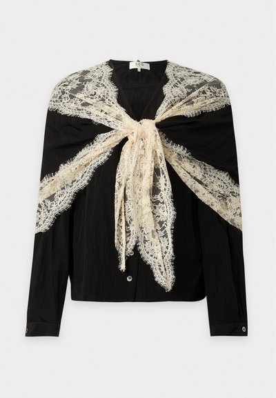 Blouse noire à manches longues avec boutons sur le devant, drapée d'un châle en dentelle florale beige noué sur les épaules et la poitrine.