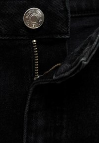 Tessuto di denim nero con dettaglio di bottone e zip metallici. La zip è di tono dorato, con denti visibili, e la cucitura è rifinita.