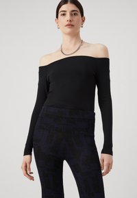 Zwarte off-the-shoulder bodysuit met lange mouwen, gecombineerd met blauwe, patroon hoge taille broek met een geribbeld textuur en subtiele glans.