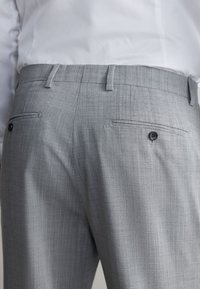 Pantaloni eleganti da donna grigi con tessuto strutturato. Presentano due tasche posteriori con bottoni neri e passanti per cintura. Design pulito e professionale.