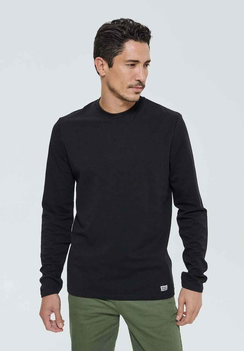 T-shirt noir à manches longues en coton avec un col rond. Présente un petit écusson logo en bas et des manches ajustées.