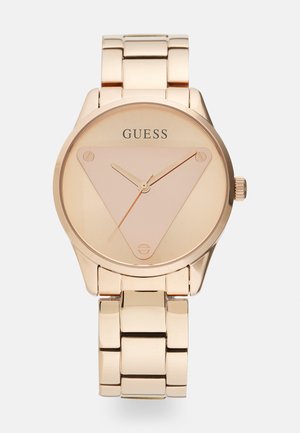 Montre en or rose avec un cadran triangulaire, au design minimaliste et à bracelet en maillons métalliques. Présente une finition lisse et polie ainsi qu'un logo en haut.