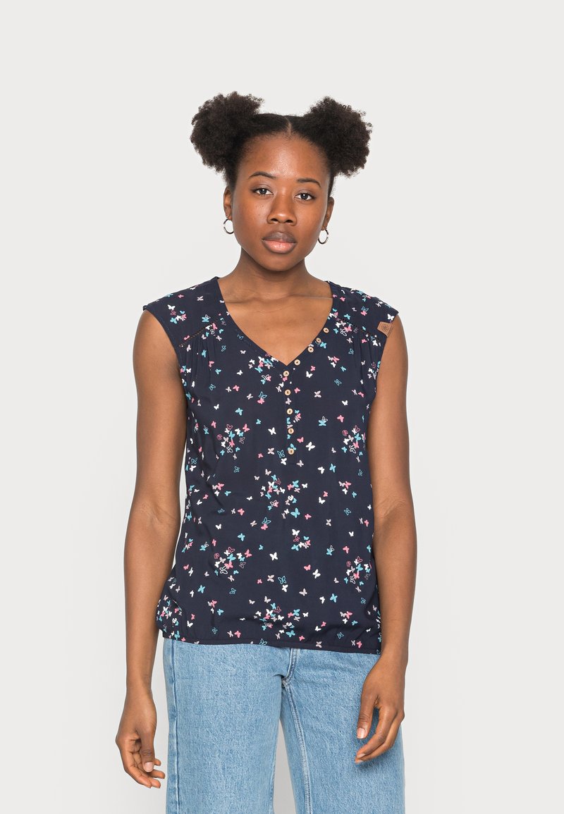 Blusa azul-marinho com mangas em formato de capa, padrão floral em rosa e azul, decote em V e detalhes em botão, combinada com jeans azul-claro.
