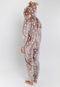 Beiger Overall mit einem plüschigen Material, das weiße herzförmige und ovale Flecken zeigt. Goldene Geweihstangen an der Kapuze verleihen ein verspieltes Detail.