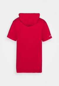 Sudadera corta roja de manga corta con capucha y corte regular. Presenta detalles de costura y un logotipo en la manga izquierda. Textura de tela suave.