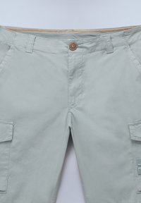 Pantaloni cargo grigi chiaro con chiusura a bottone, tasche frontali doppie e dettagli con zip arancione a contrasto in vita.