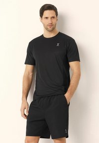 Zwarte sport T-shirt met korte mouwen, ronde halslijn en vochtafvoerende stof; gecombineerd met bijpassende zwarte shorts.