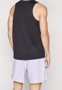 Débardeur noir sans manches avec un motif texturé, associé à un short violet clair, offrant une coupe décontractée et un tissu lisse.