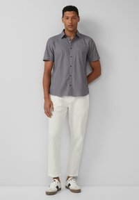 Grijze shirt met korte mouwen en knoopsluiting, borstzak en witte broek, gecombineerd met witte en beige sneakers. Glad stofgevoel.