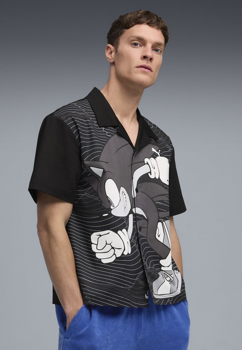 Sortærmet sort skjorte med Sonic the Hedgehog grafik; har hvide linjer og en glat tekstur; klassisk kravedesign.