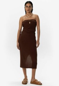 Bruine geribbelde gebreide jurk met een strapless ontwerp en een lengte tot halverwege de kuit. Gepaard met tan flat sandals met decoratieve stiksels.