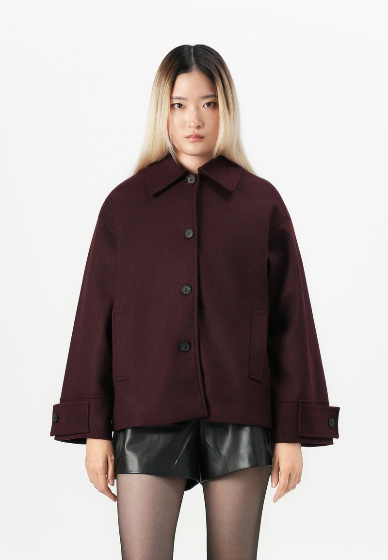 Veste en mélange de laine bordeaux avec un large col, fermeture à boutons sur le devant et poches latérales. Présente une coupe ample et des poignets surdimensionnés.