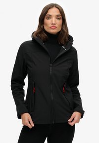 Schwarze Softshell-Jacke mit Reißverschluss vorne, verstellbarer Kapuze und orangefarbenen Akzenten an zwei Seitentaschen; glatte Textur und figurbetontes Design.