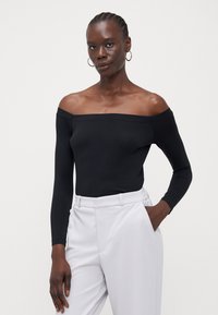 Svart av-og-skulderen langermet bodysuit laget av glatt stoff; parret med lysegrå høy midje bukser; minimalistisk design.