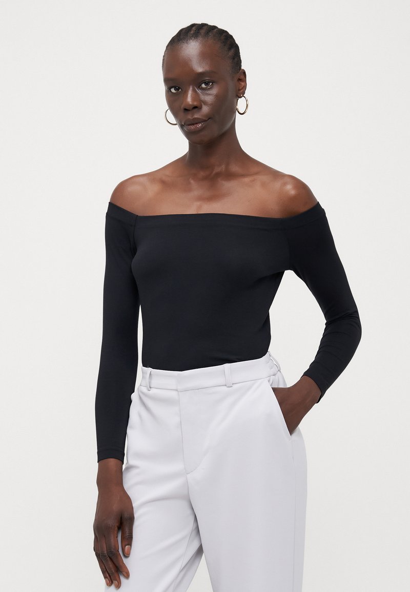 Svart av-og-skulderen langermet bodysuit laget av glatt stoff; parret med lysegrå høy midje bukser; minimalistisk design.