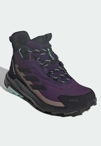 Purple hiking shoes with black accents, textured mesh upper, and rubber outsole featuring green detailing. Designed for wet conditions.