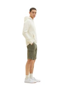 Lys cremefarvet hoodie med frontlomme, parret med olivengrøn cargo shorts med sidelommer, hvide sneakers og lyse sokker.