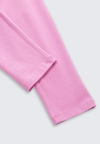 Hellrosa Stoff mit glatter Textur und gleichmäßig genähten Säumen, der ein passgenaues Design mit langen Ärmeln zeigt.