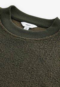 Olivgrüner Fleece-Pullover mit strukturiertem Finish, geripptem Kragen und einem Etikett mit der Aufschrift "NEXT", Größe M, aus weichem, warmem Material.