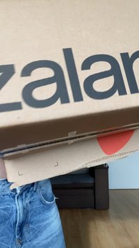 Ruske pahılı kutije složene jedna na drugu, sa velikim crnim tekstom "zalando." Jedna kutija ima crveni okrugli detalj. Uočava se svetli drveni pod.