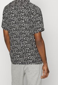 Krátký rukáv košile z lehkého materiálu s šedým základem a černým leopardím vzorem; má klasický límeček a volný střih.